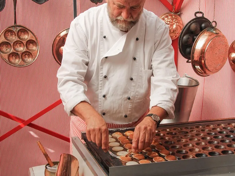 Koch bei der Zubereitung kleiner Pfannkuchen an der Kochstation Koch bei der Zubereitung kleiner Pfannkuchen an der Kochstation